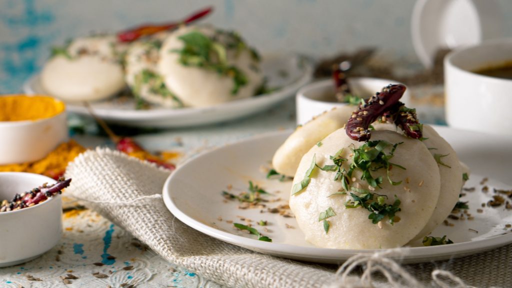 Plate of Indian Idli rice cakes served on table with herbs and sun dried chili pepper