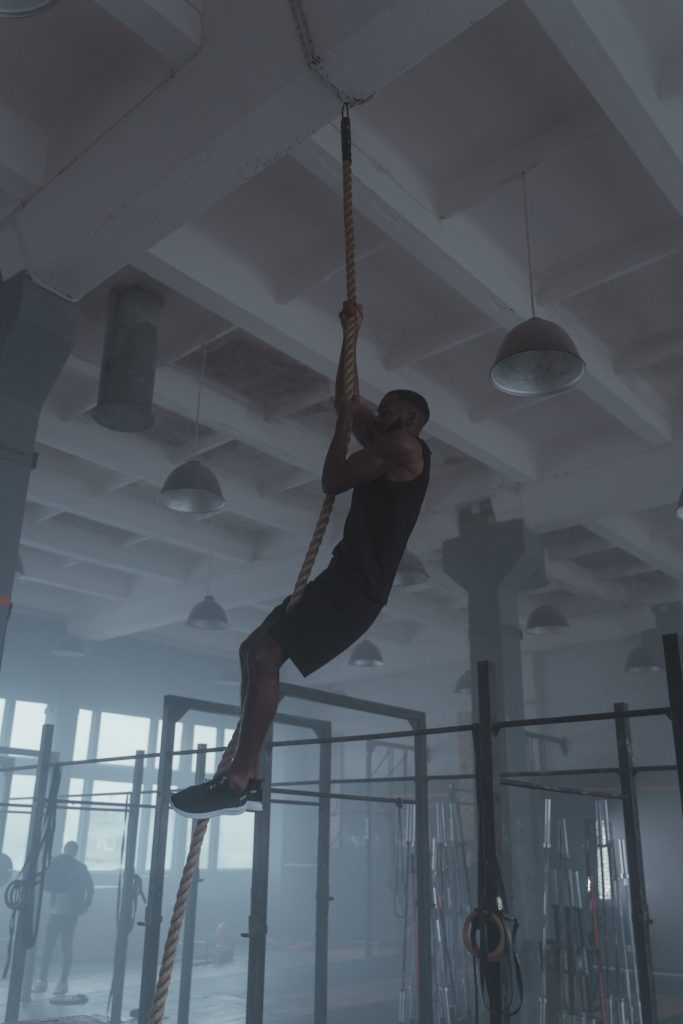 Man climbing a rope in a gym, showcasing strength and fitness in a modern indoor setting.
